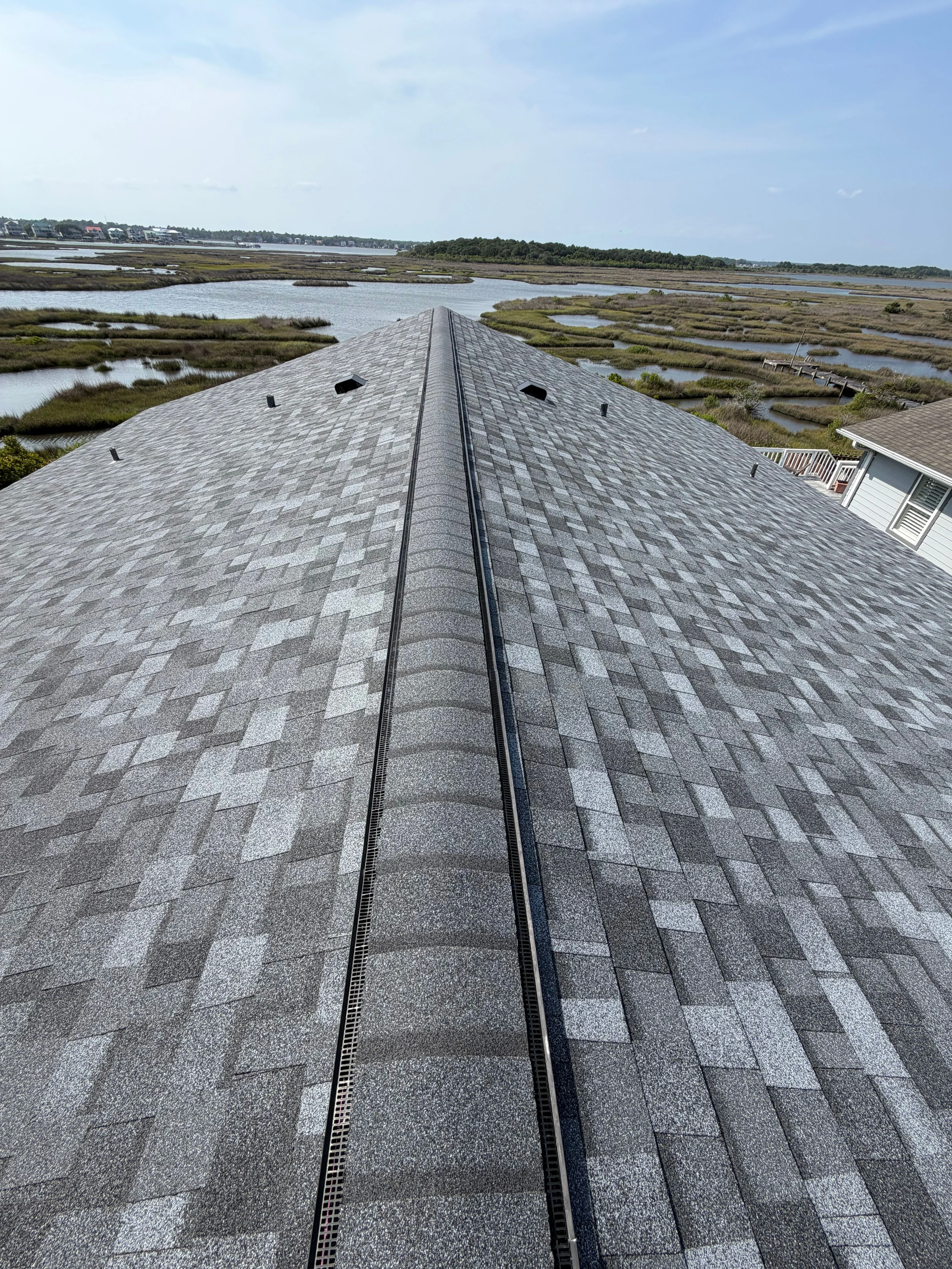 Aerial view of a residential roof replacement in progress in Craven County, NC, with the Neuse River visible in the background and new architectural shingles being installed on a coastal home.
